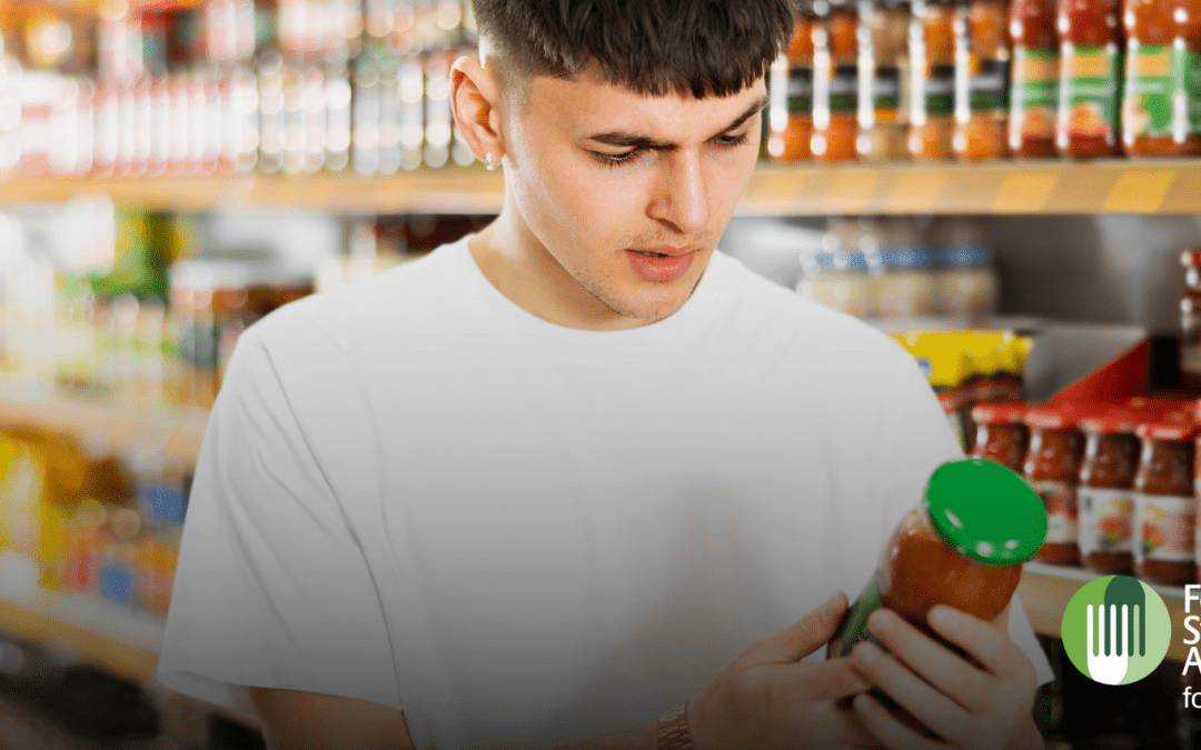 Young man looking at the label of a jar of sauce in a supermarket